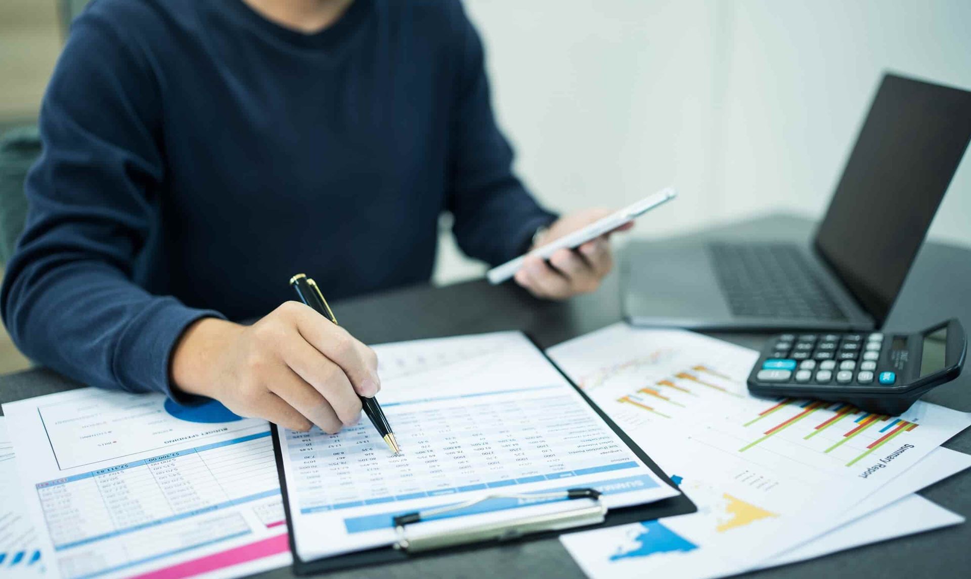 A Man Is Sitting at A Table Using a Tablet and A Calculator — Blue Orchid Accounting In Woongarrah, NSW