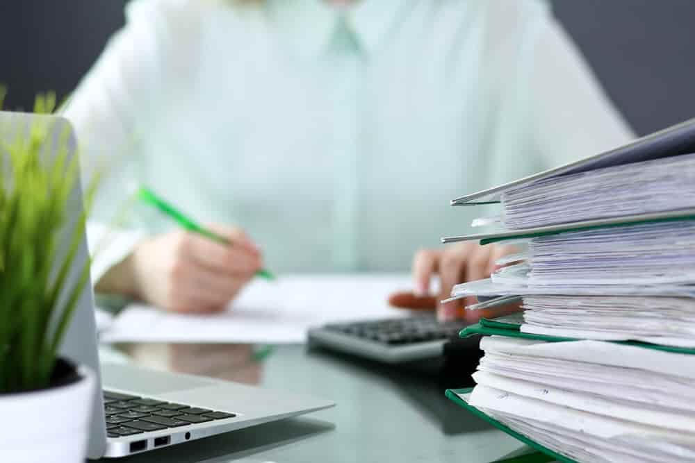 A woman is sitting at a desk using a laptop and a calculator — Blue Orchid Accounting In Woongarrah, NSW