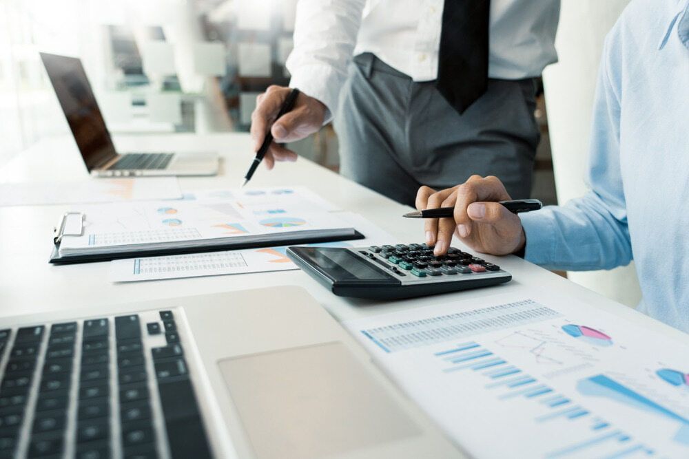 Two Men Are Sitting at A Table with A Laptop and A Calculator — Blue Orchid Accounting In Woongarrah, NSW