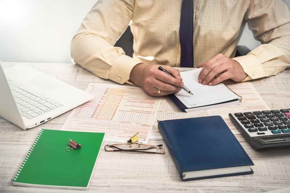 A Man Is Sitting at A Desk Writing on A Piece of Paper — Blue Orchid Accounting In Woongarrah, NSW