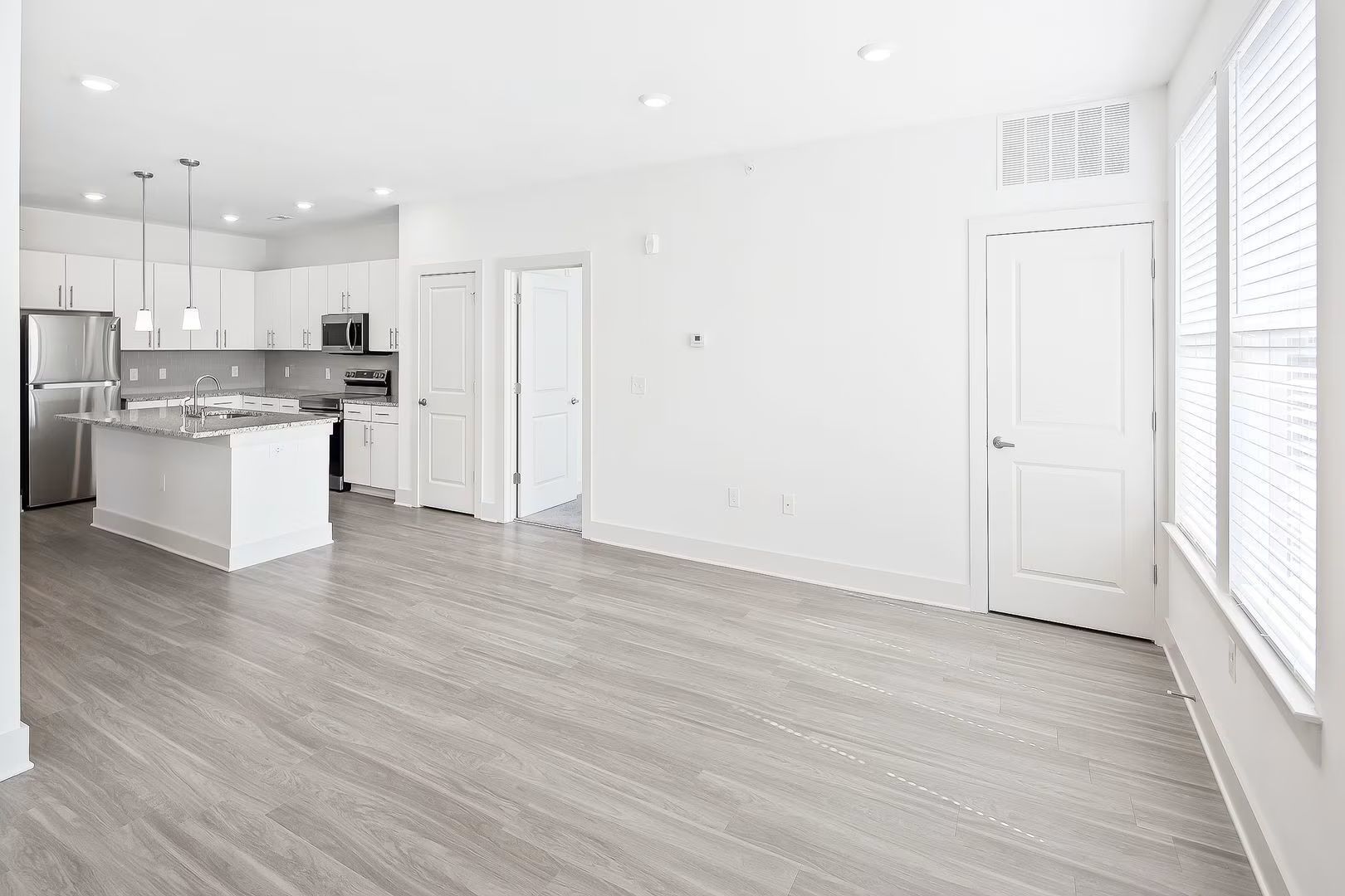 Open-concept living space with white walls, gray wood floors, and a white kitchen island.