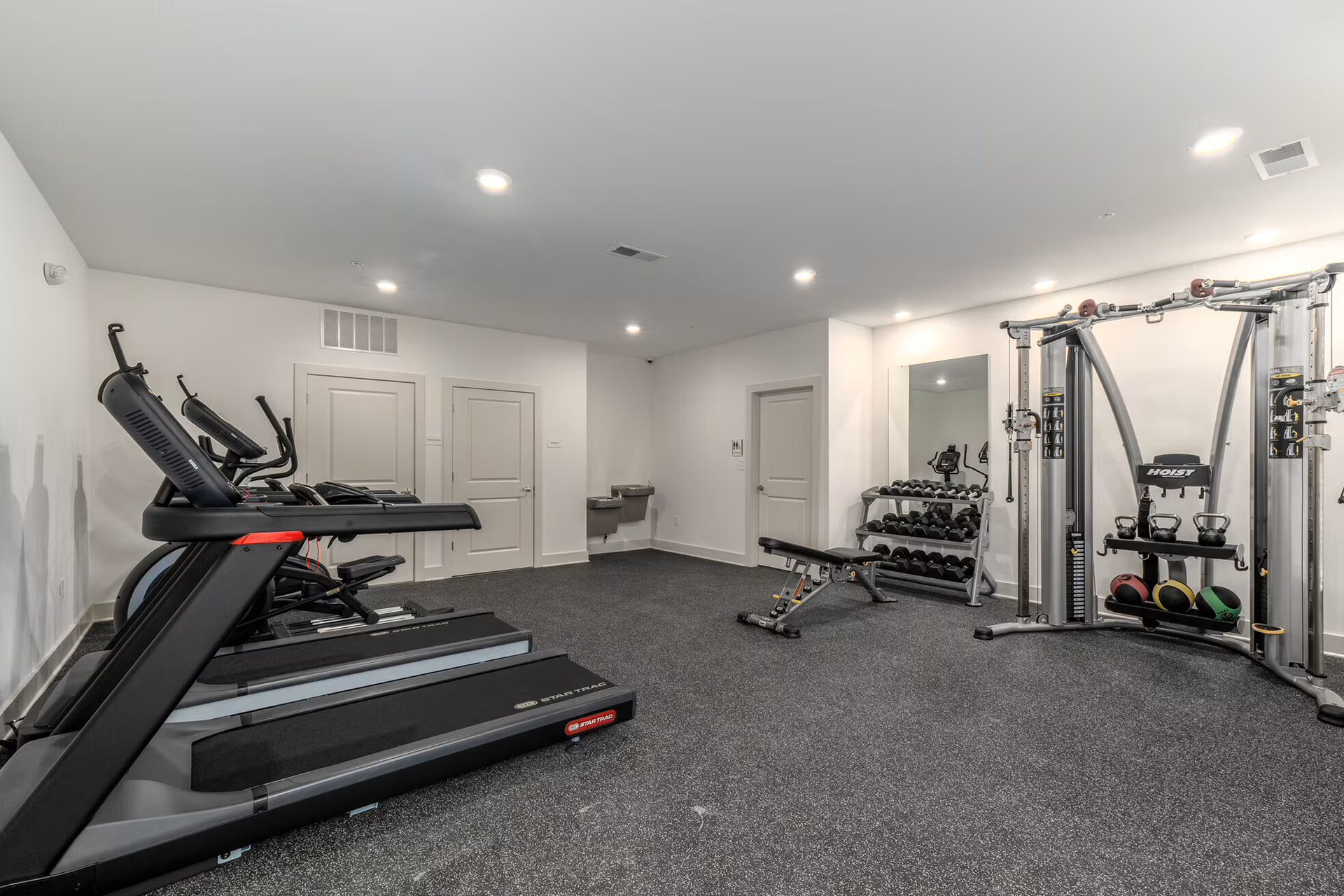 Gym with treadmill, exercise bike, weights, and cable machine on a dark floor.