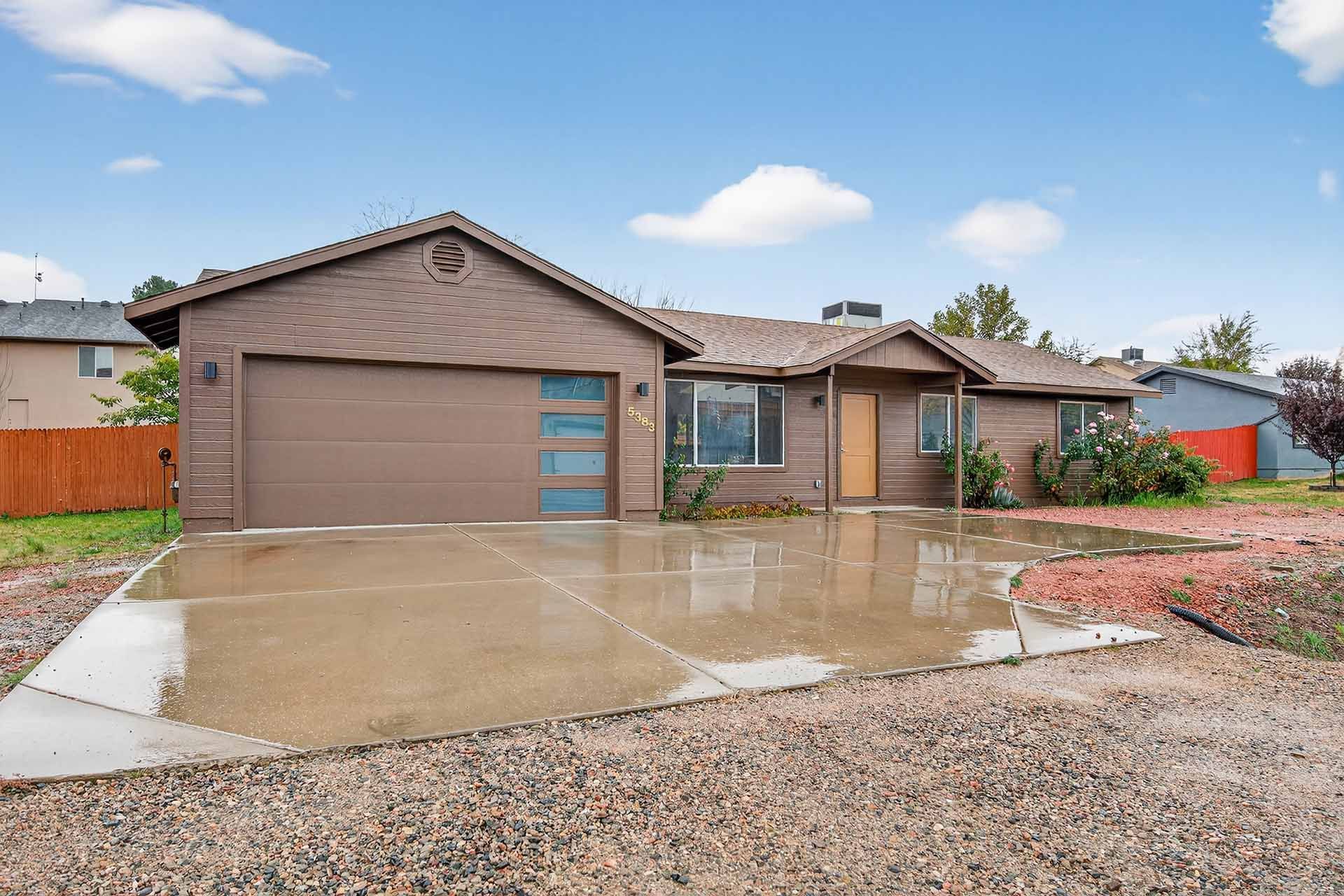 Single-story house with brown garage and wet driveway after rain, under a blue sky