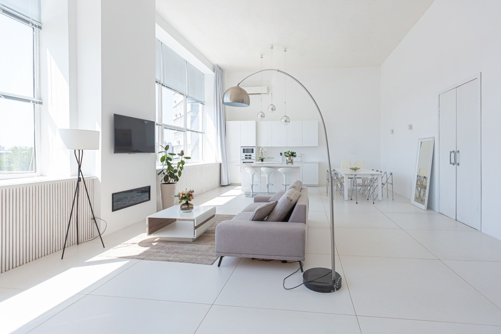 Minimalist bright living room with gray sofa, white walls, large windows, and a floor lamp
