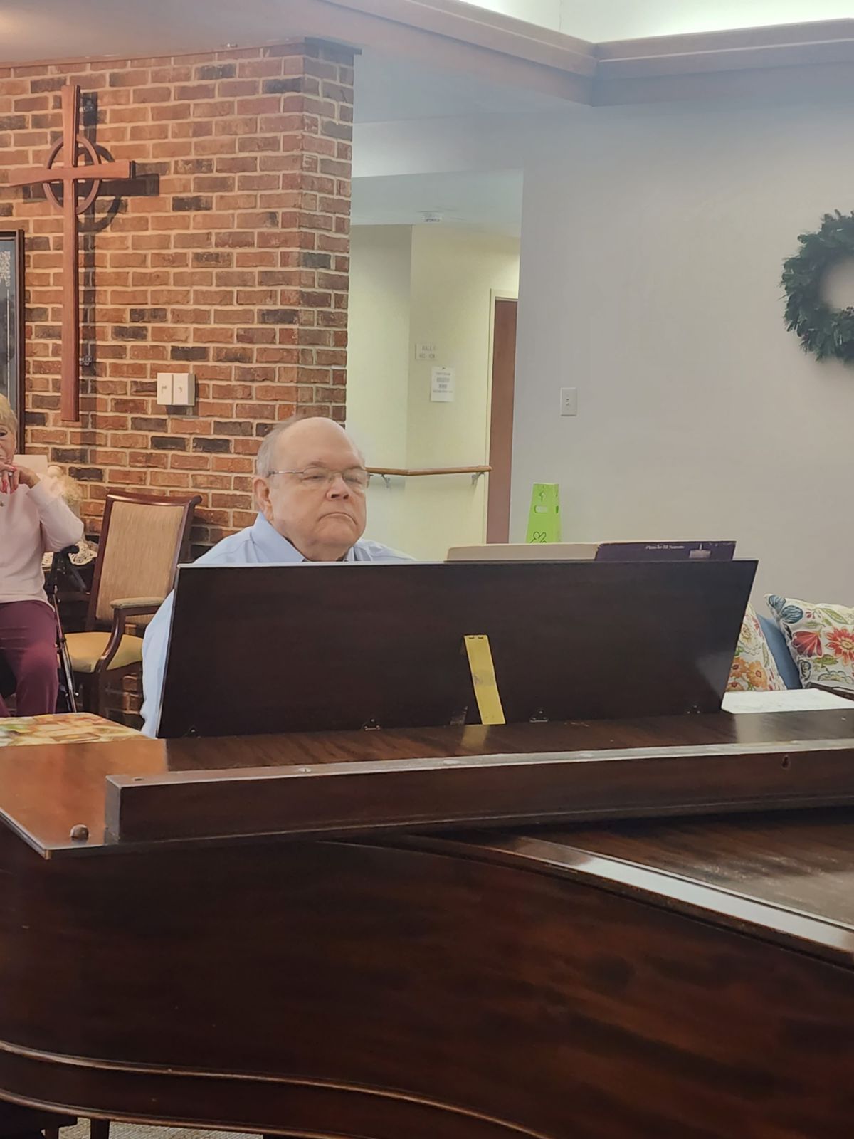 Man seated at a piano in a brick church sanctuary, with a cross and wreath in the background