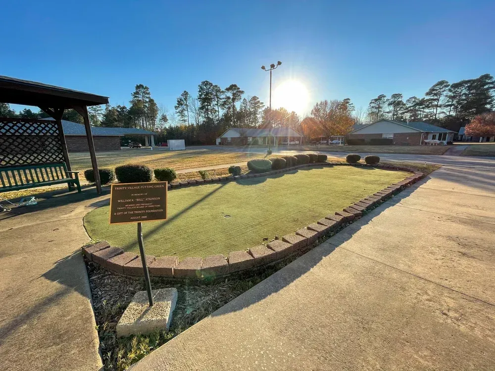 Sunlit park walkway with a small brick memorial and sign, surrounded by grass and trees