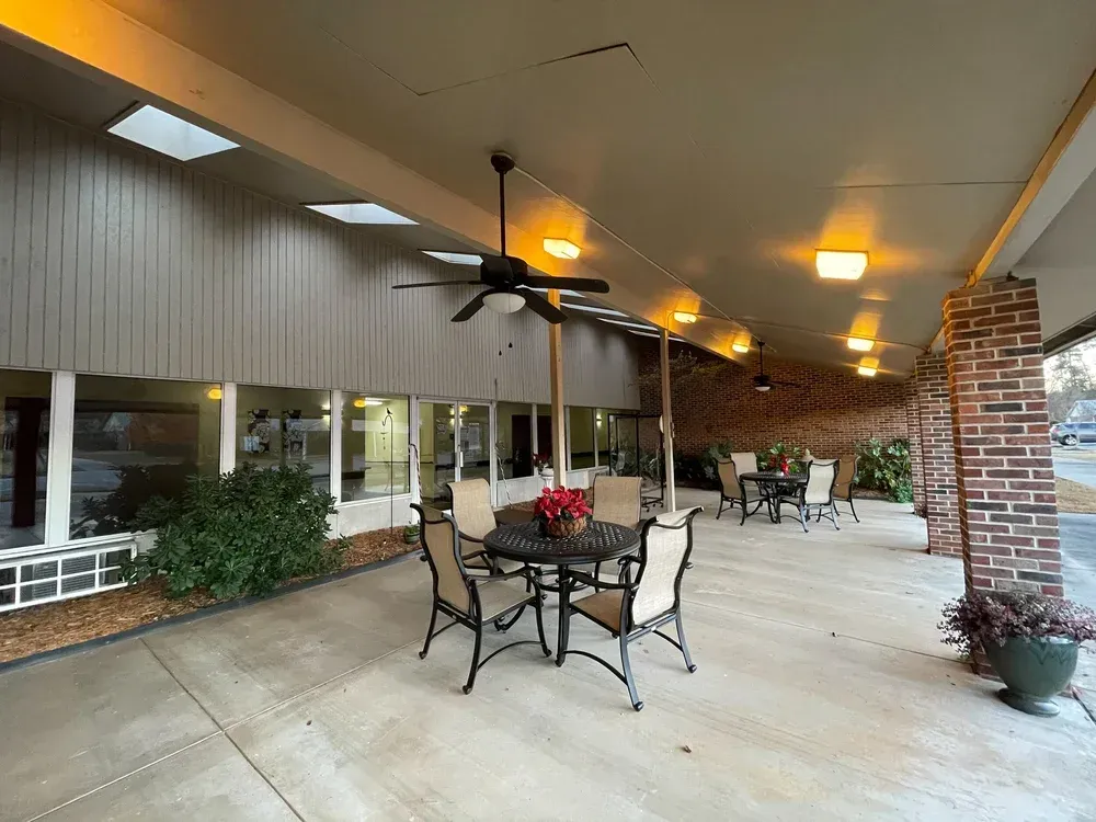 Covered outdoor patio with tables, chairs, ceiling fans, and warm lights along a brick wall