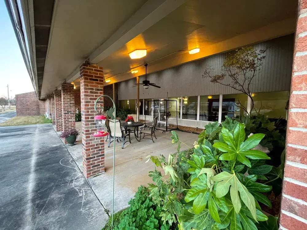 Outdoor café seating under an awning beside a brick building, with tables, chairs, and potted plants