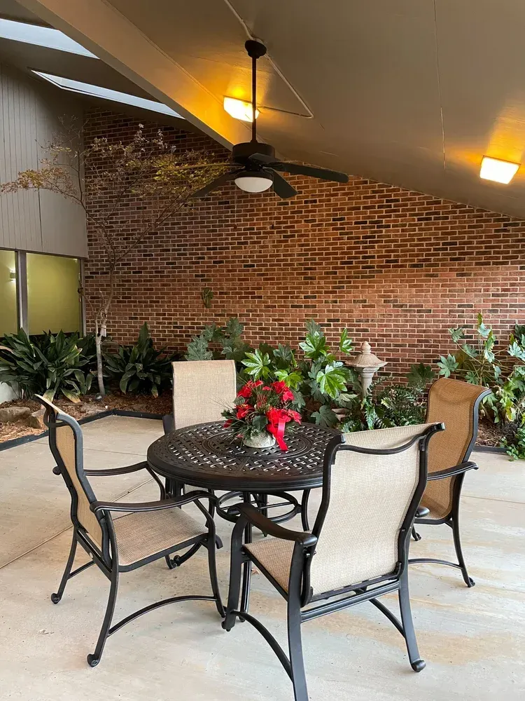 Patio dining area with round table, chairs, plants, and brick wall under warm ceiling lights