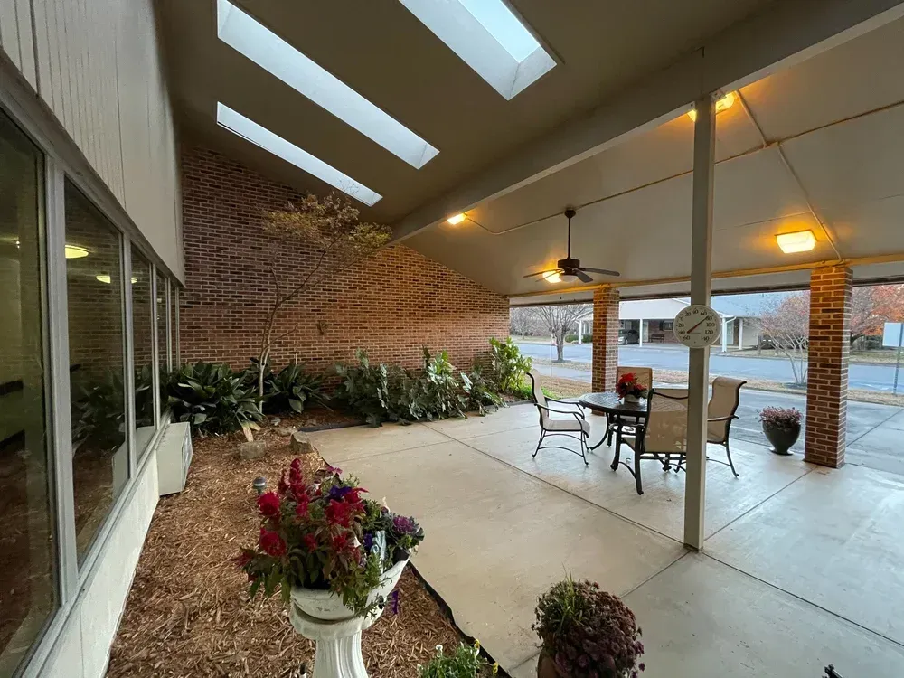 Covered patio with skylights, white columns, brick wall, and outdoor tables with potted flowers