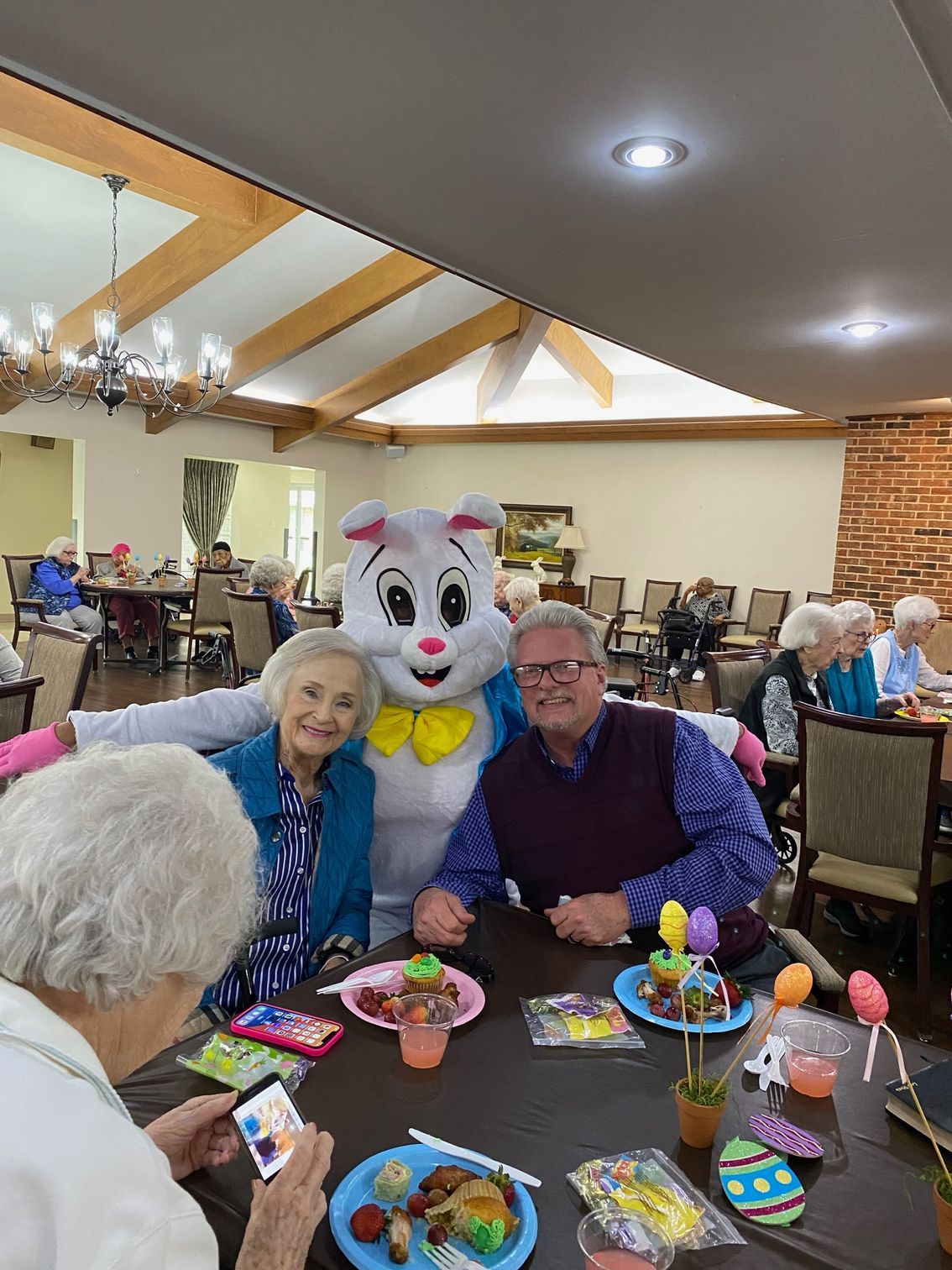 Easter bunny mascot posing with two seated guests at a festive dining table in a banquet hall