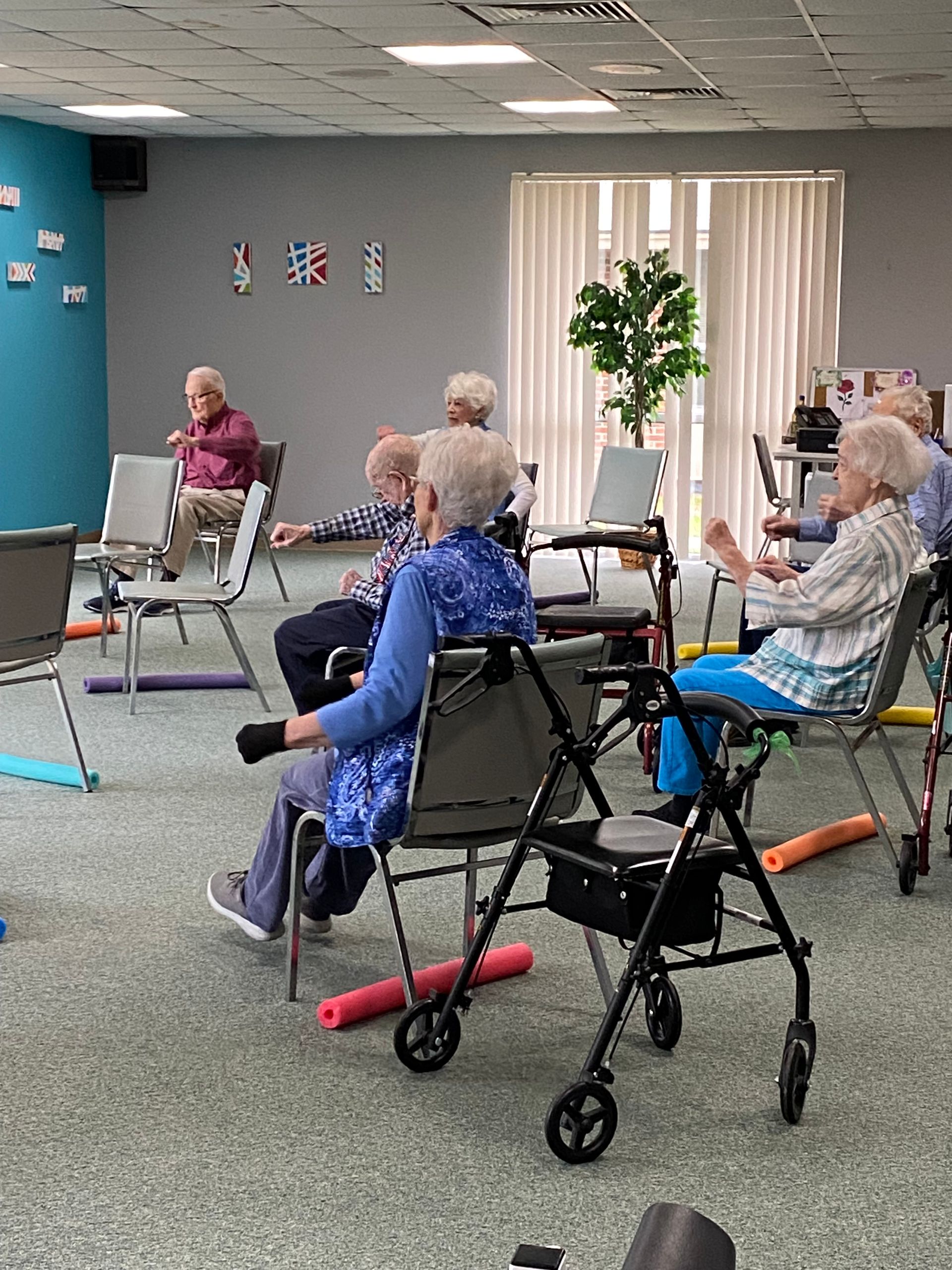 People seated in walkers during a group exercise class in a community room