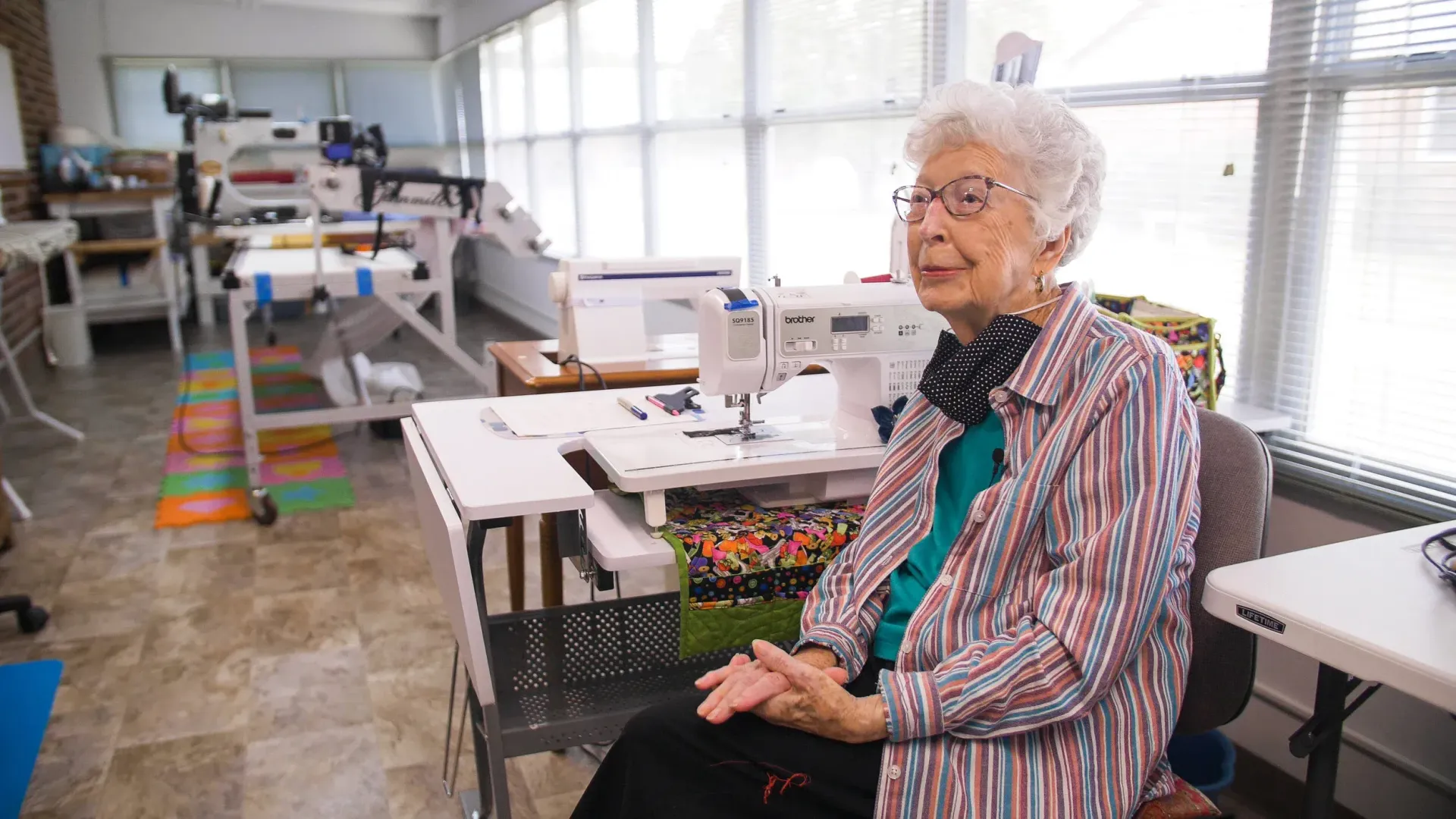 Woman seated at a sewing machine in a bright studio with tables and craft supplies