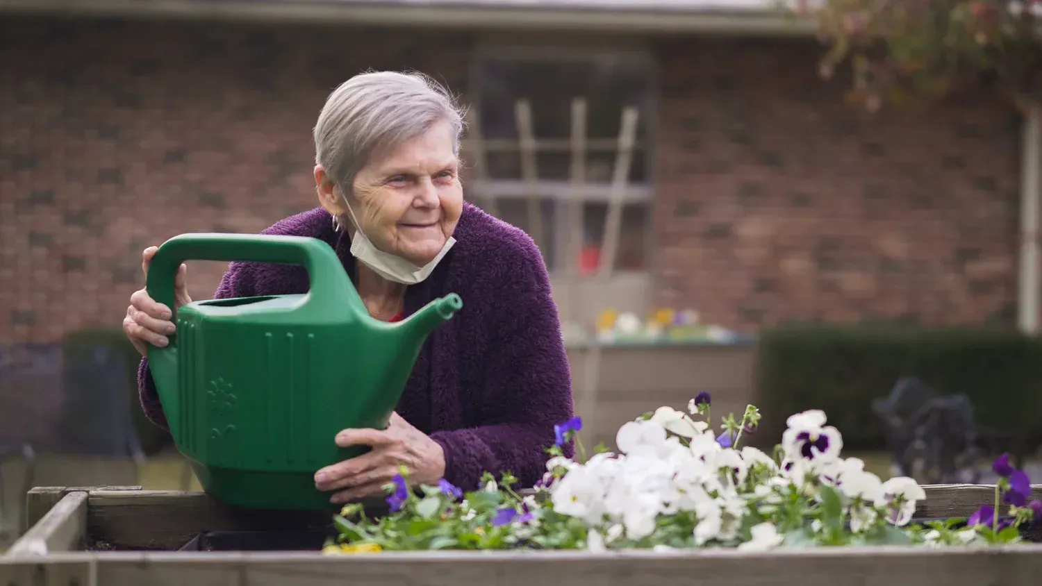 Woman watering flowers in a garden with a green watering can and smiling face