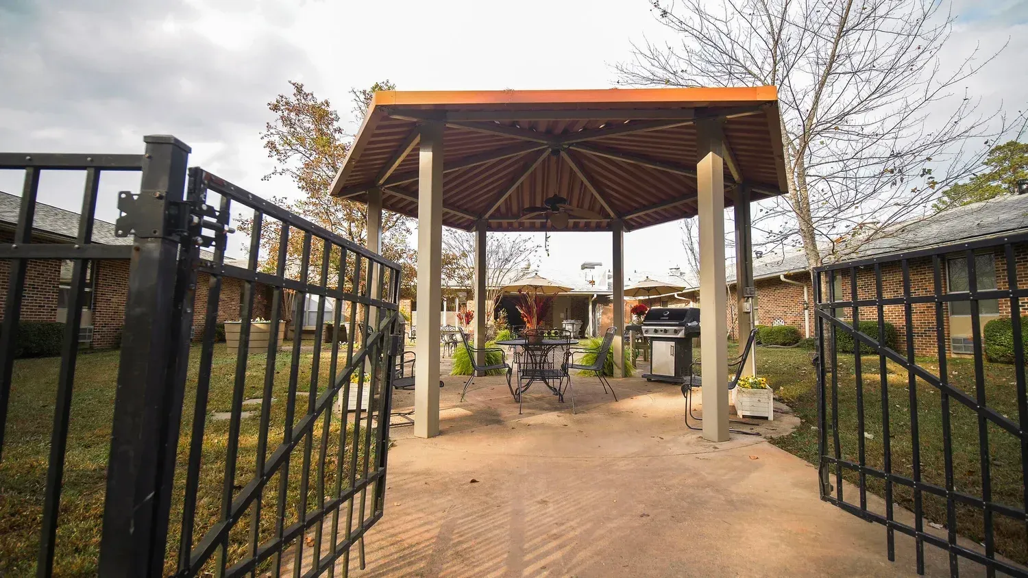Open gate leading to a courtyard with a wooden pavilion and outdoor seating