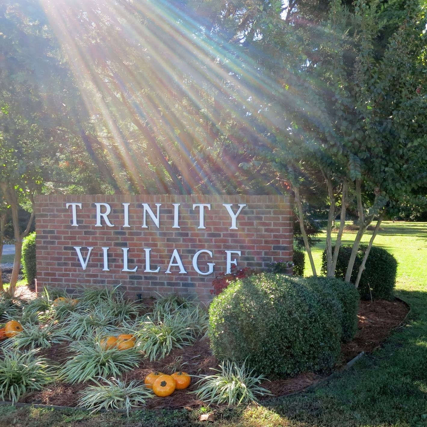 Trinity Village brick sign in a sunlit landscaped garden with pumpkins and greenery