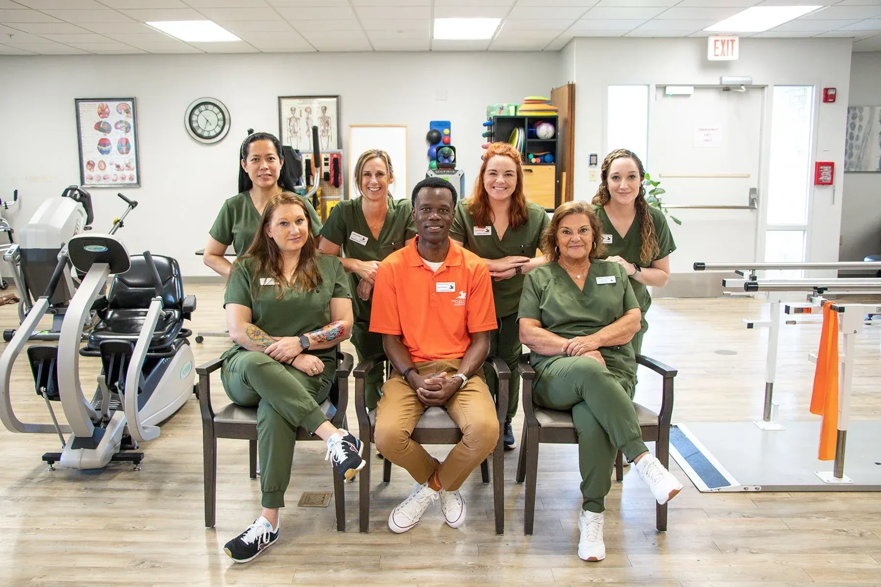 Group of medical staff in green scrubs posing in a rehab clinic with exercise equipment