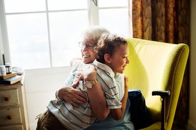 Family relaxing on a couch by a window, talking and laughing. Soft light fills the room.