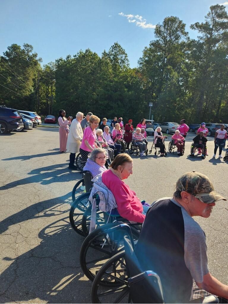 People in pink shirts gathered outdoors with wheelchairs in a parking lot near trees and parked cars