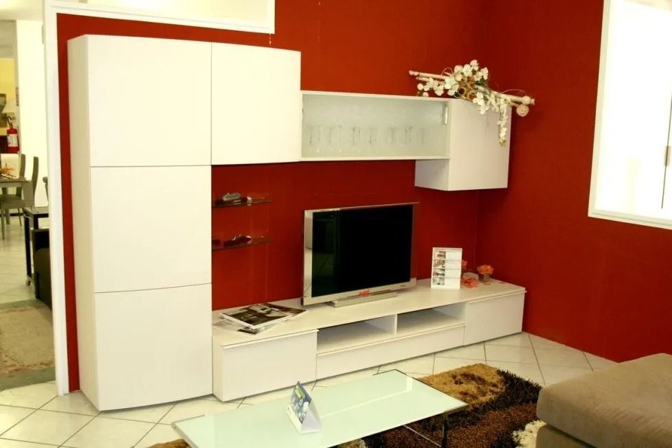 Mobiletto moderno bianco per l'intrattenimento contro una parete rossa con TV, scaffali e armadietti.
