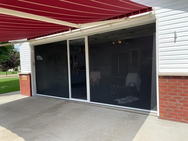 Closed screened patio with dark mesh panels, red awning, and brick siding on a house