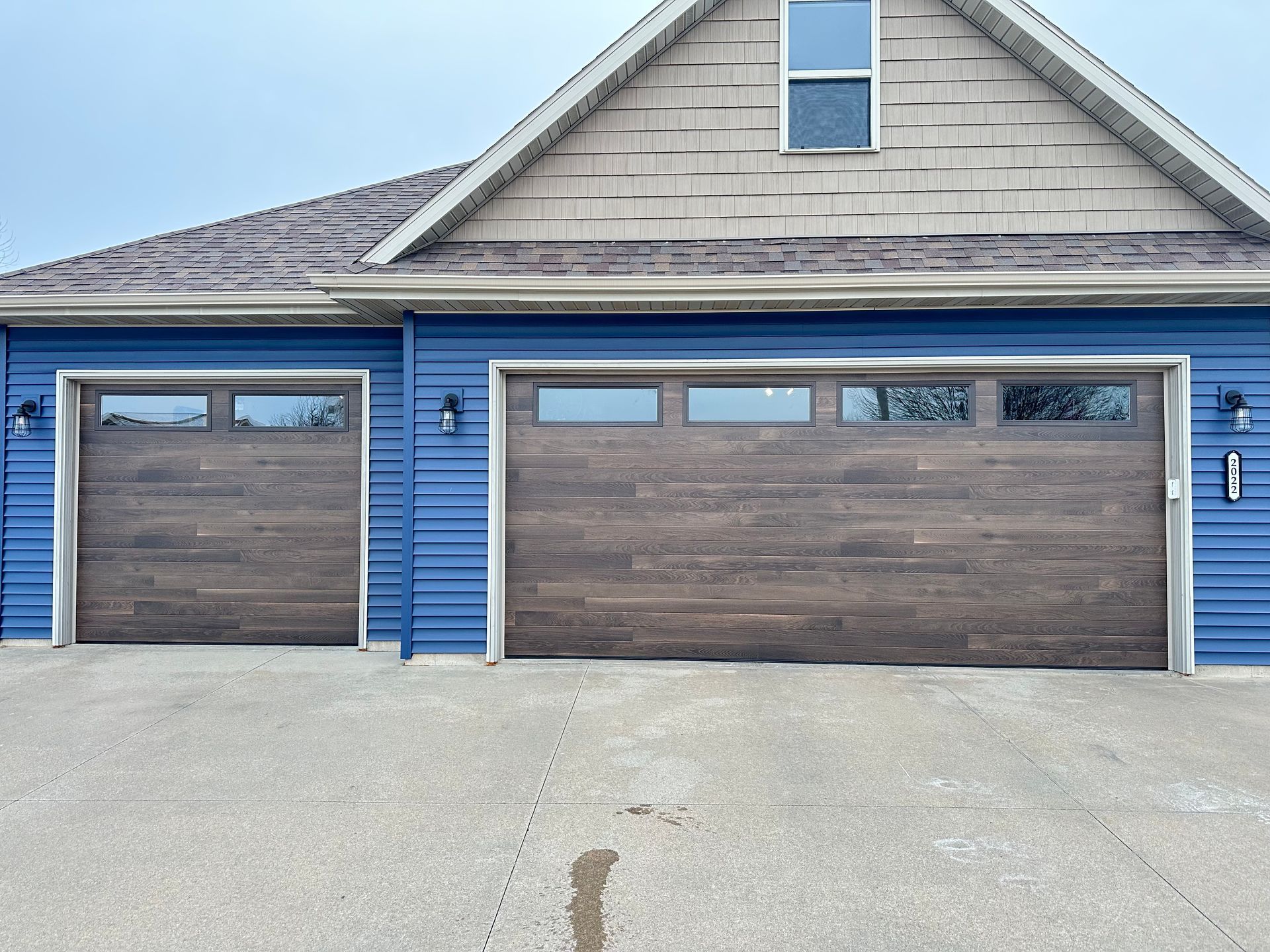 Two wood-look garage doors on a blue-sided house with a paved driveway