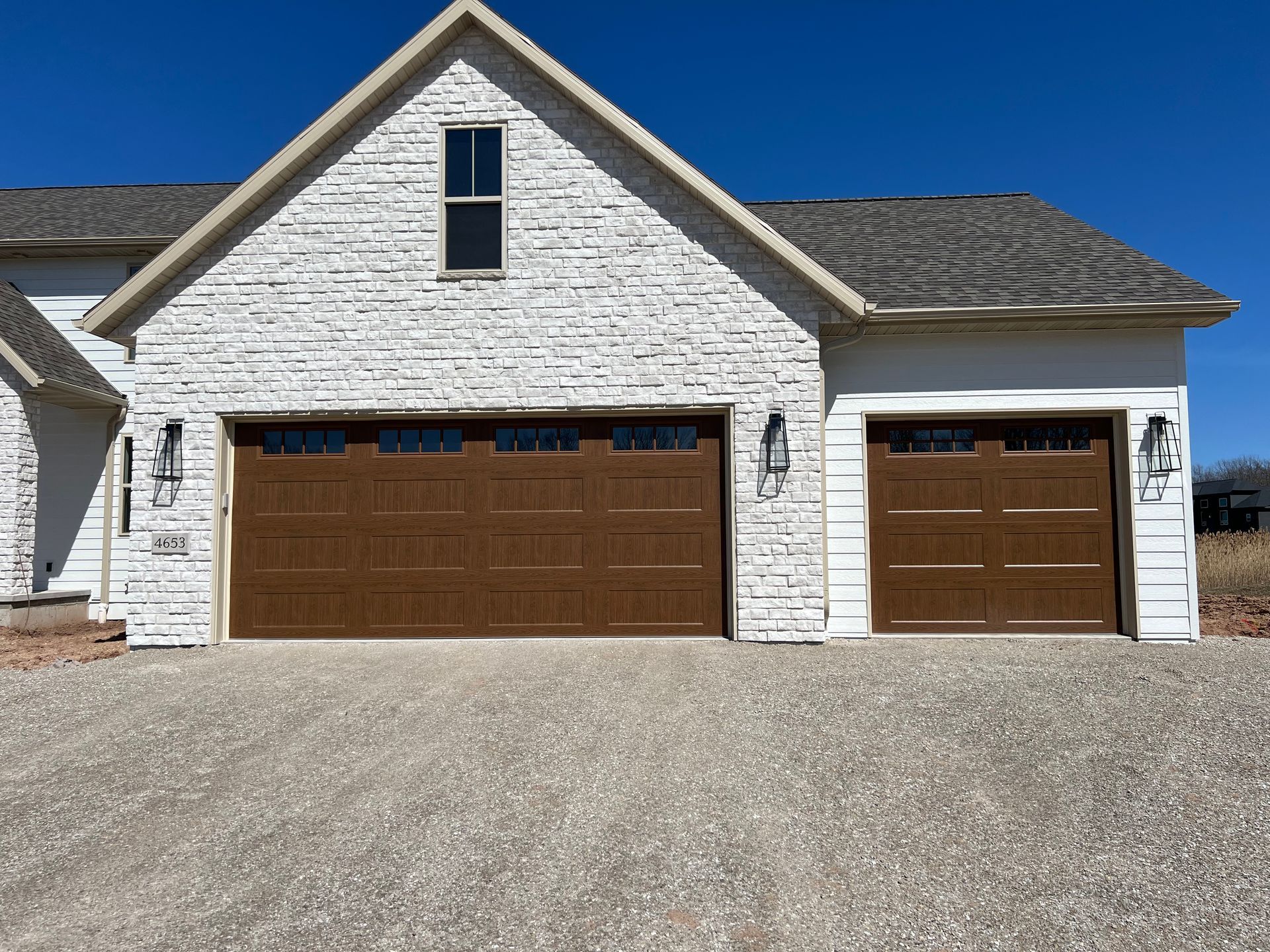 White brick suburban house with two brown garage doors and a gravel driveway