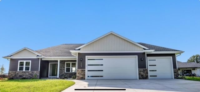 Single-story gray house with a two-car garage and a bright green lawn under a blue sky
