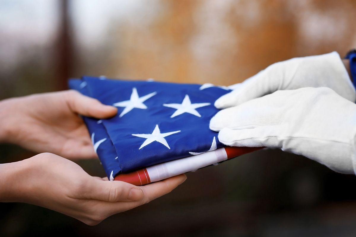 Hands in white gloves folding a folded American flag with white stars on blue and red stripes