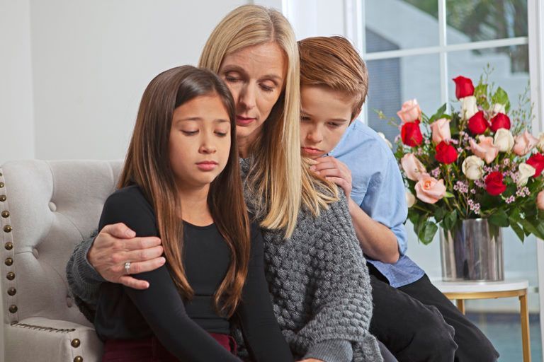 Woman comforting two children on a couch beside a vase of flowers