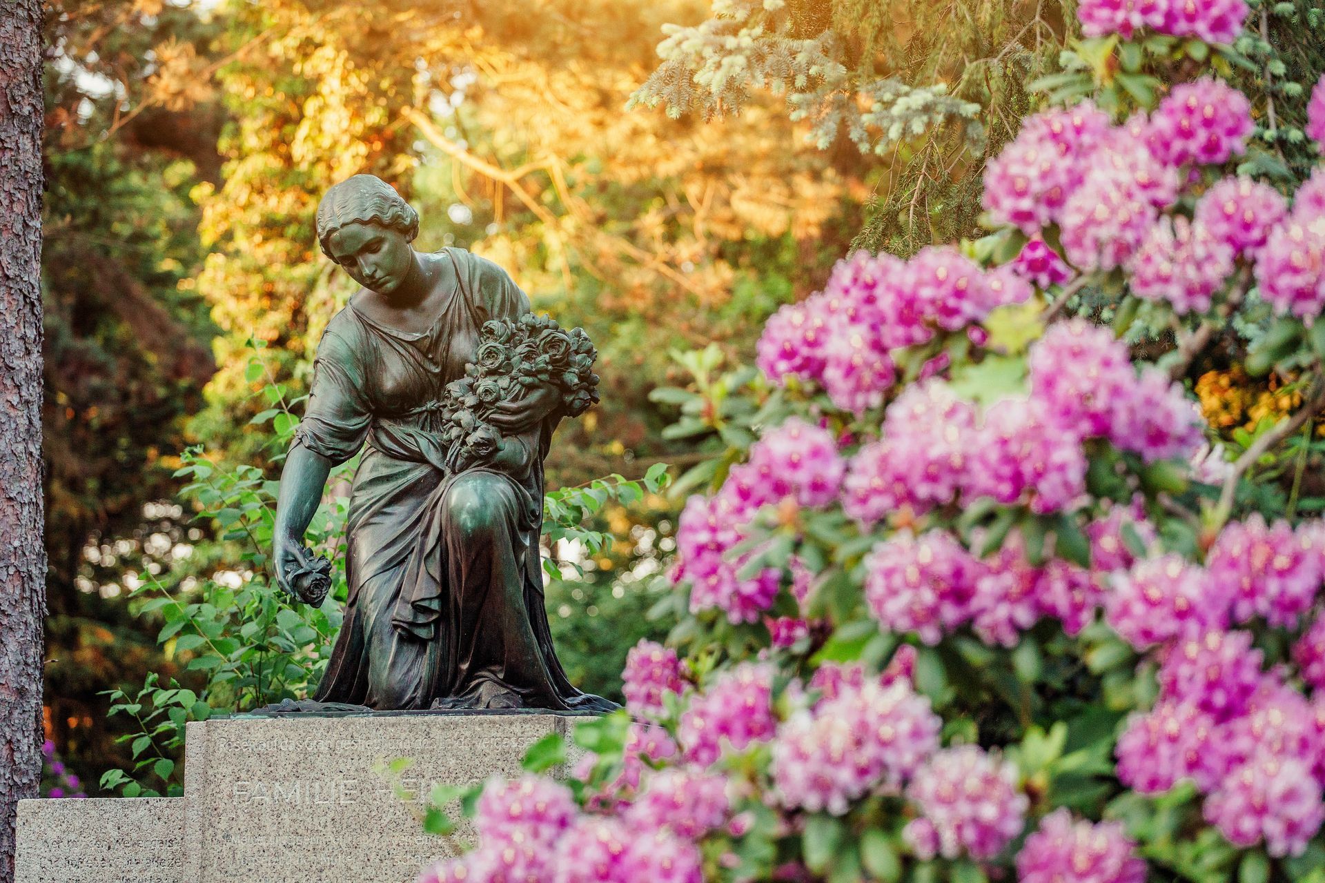 Bronze statue in a garden, framed by pink flowers and autumn foliage