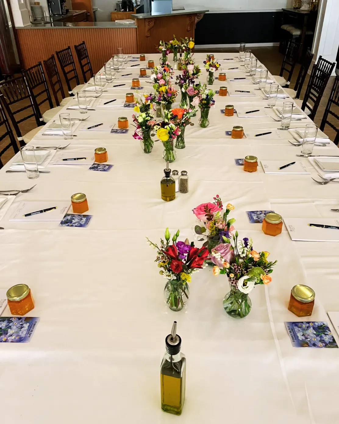Long banquet table with white cloth, colorful floral centerpieces, and place settings in a dining hall