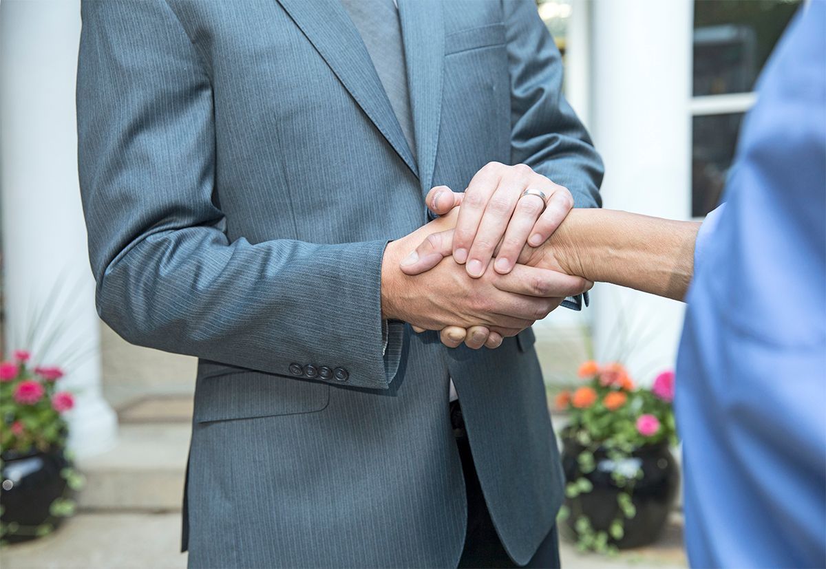 Two people in business attire shaking hands in front of a building