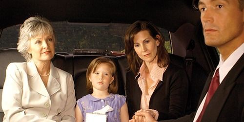 Four people seated in a car, looking toward the camera with serious expressions.
