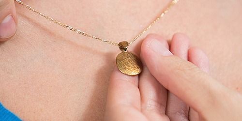 Hand adjusting a gold pendant necklace on a neck