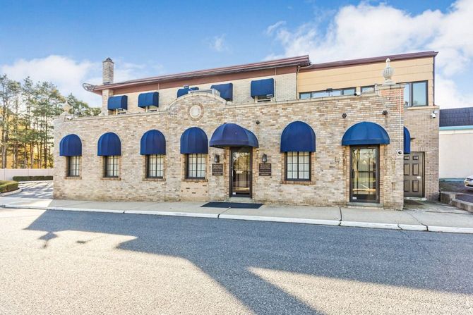 A two-story building with tan stone facade, blue arched awnings over windows and doors, and a paved parking lot in front.