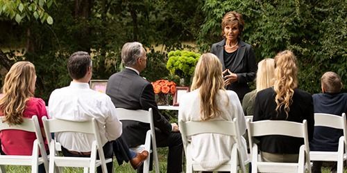Outdoor ceremony with an officiant speaking to seated guests in a garden setting