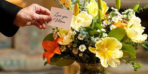 Hand placing a sympathy card on a yellow-and-white floral arrangement