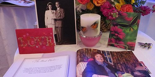 Memorial display with photos, candles, flowers, and a framed love sign on a table
