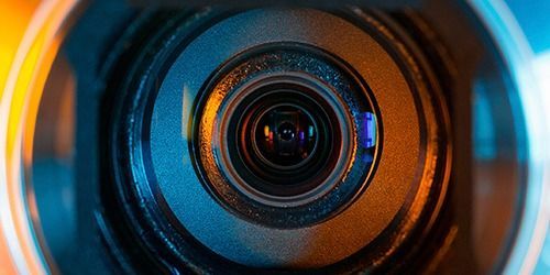 Close-up of a camera lens with orange and blue reflections on the glass