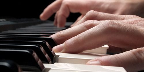 Hands playing a piano keyboard, with close-up view of the keys and fingers.