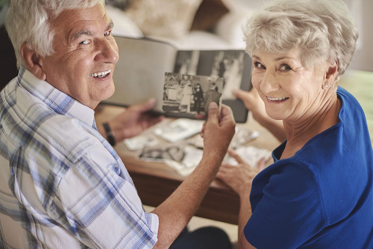 Smiling couple sitting at a table, looking at a photo in a cozy home setting.