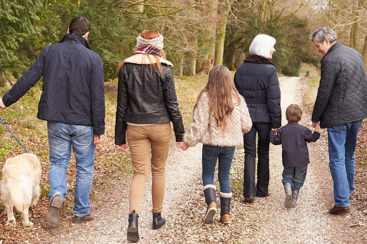 Family walking with a dog on a gravel path through a wooded park in autumn