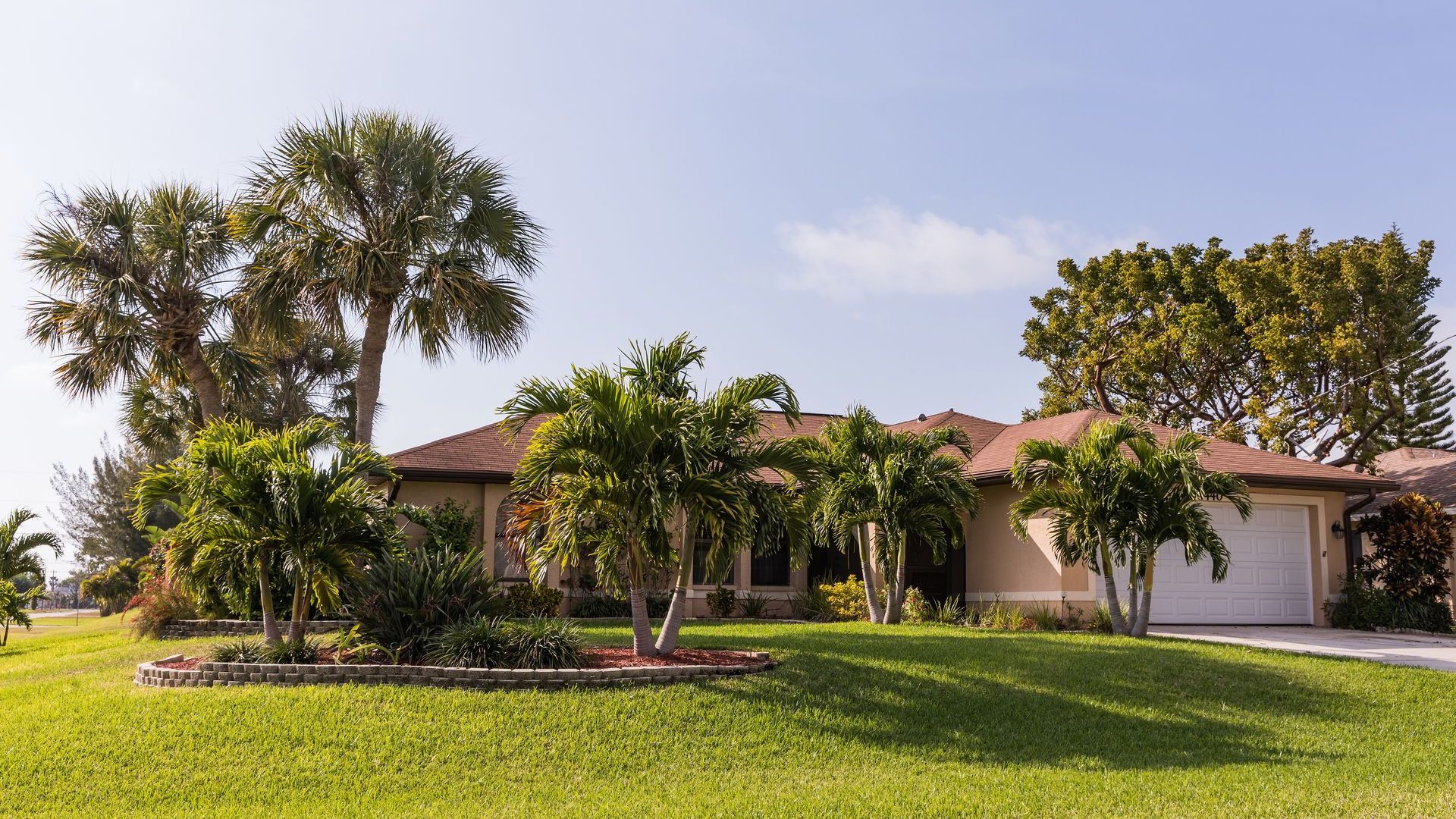 A house with a lush green lawn and palm trees in front of it.