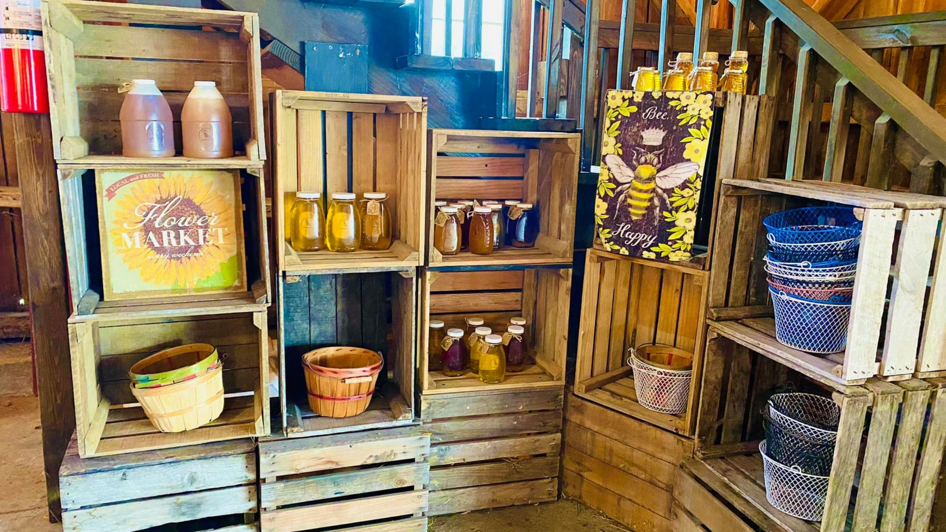 Wooden crates display jars of honey and crafts in a rustic setting, with a bee-themed sign.