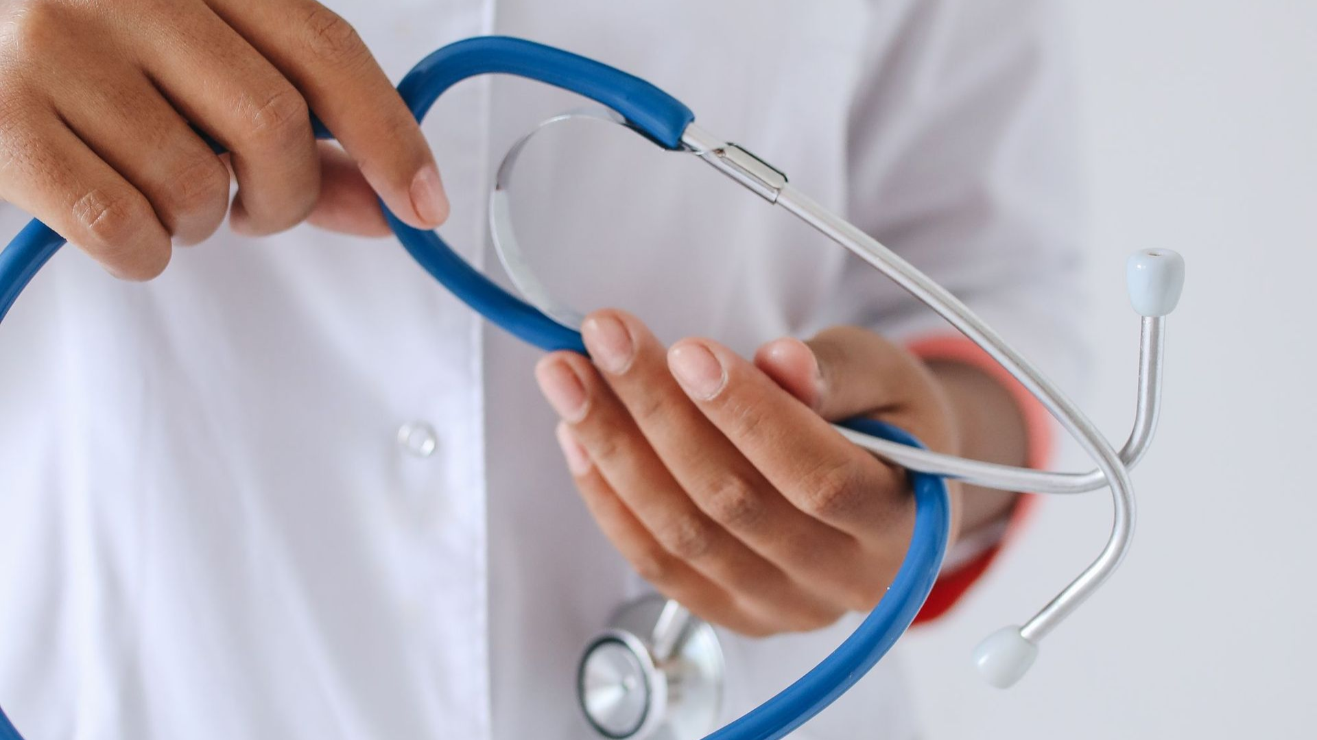 pair of hands holding a blue stethoscope, person wearing white lab coat