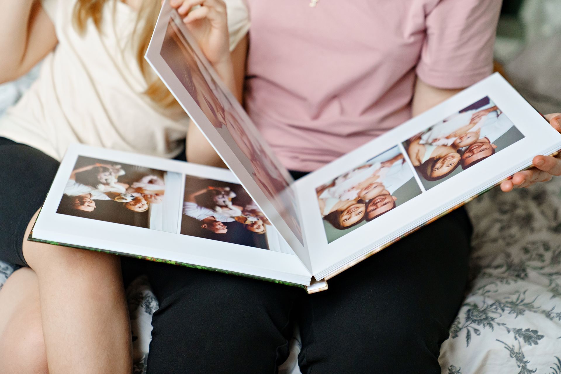 Two people looking at a photo album with family photos on a bed.
