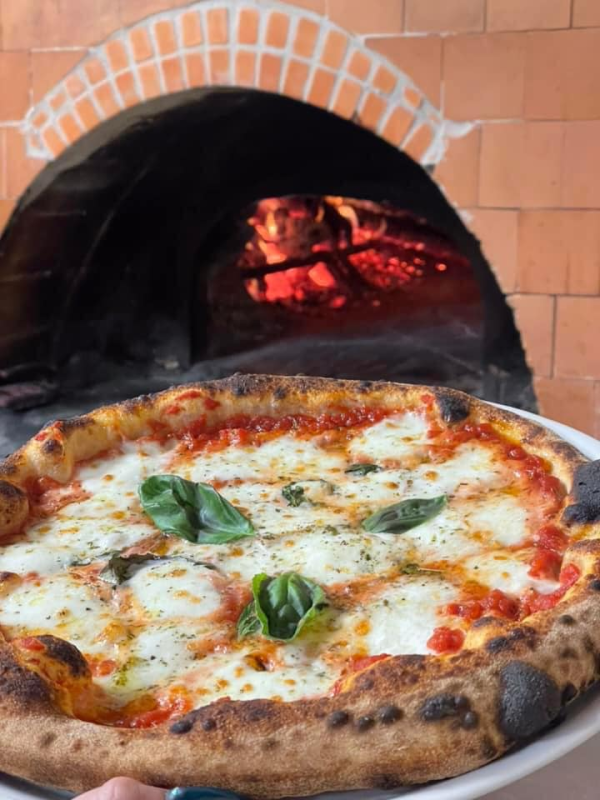 Pizza cotta in un forno a legna in mattoni con braci ardenti e foglie di basilico in cima