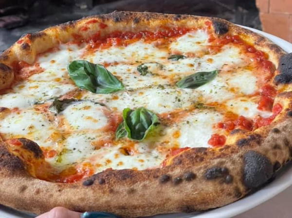 Pizza napoletana con mozzarella fusa, foglie di basilico e besciamella su un piatto