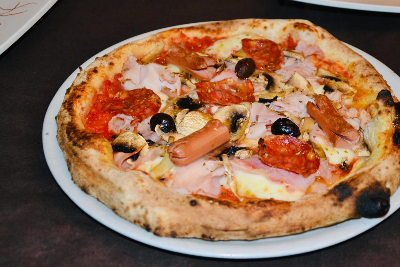 Pizza su un piatto bianco con olive, peperoni, prosciutto e formaggio fuso su un tavolo